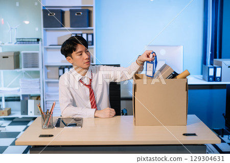 Asian male professional packing office belongings in a box, representing themes of resignation, new job, 129304631