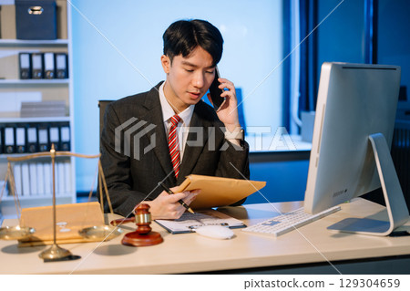 Business professional in suit discussing legal documents over phone, showcasing a formal office setting with a focus Business professional in suit discussing legal documents over phone, showcasing a formal office setting with a focus 129304659