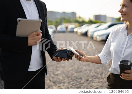 A car dealer assisting a female customer with a purchase, using a mobile payment system at a car dealership. A car dealer assisting a female customer with a purchase, using a mobile payment system at a car dealership. 129304695
