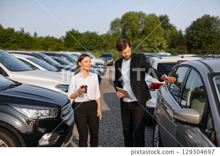 A car dealer is showing a new car to a woman. The car is a silver color. 129304697