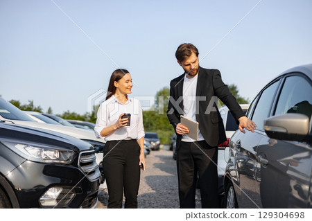 A male car dealer showing a car to a woman customer at a dealership. 129304698