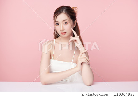 A beautiful young Asian woman with clean, fresh skin against a pink background. Skincare, facial treatment, cosmetology, beauty, and spa. An elegant portrait of an Asian woman. A beautiful young Asian woman with clean, fresh skin against a pink background. Skincare, facial treatment, cosmetology, beauty, and spa. An elegant portrait of an Asian woman. 129304953