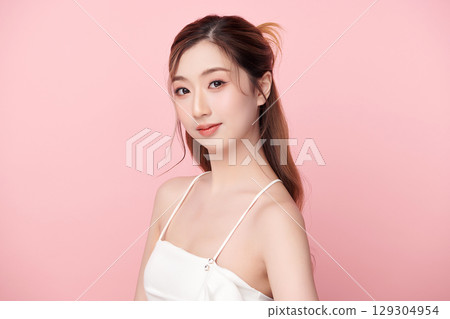 A beautiful young Asian woman with clean, fresh skin against a pink background. Skincare, facial treatment, cosmetology, beauty, and spa. An elegant portrait of an Asian woman. 129304954