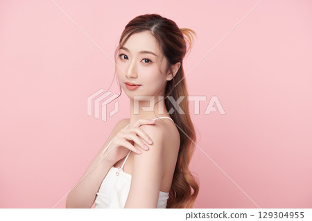A beautiful young Asian woman with clean, fresh skin against a pink background. Skincare, facial treatment, cosmetology, beauty, and spa. An elegant portrait of an Asian woman. 129304955