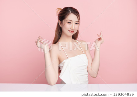 A beautiful young Asian woman with clean, fresh skin against a pink background. Skincare, facial treatment, cosmetology, beauty, and spa. An elegant portrait of an Asian woman. A beautiful young Asian woman with clean, fresh skin against a pink background. Skincare, facial treatment, cosmetology, beauty, and spa. An elegant portrait of an Asian woman. 129304959