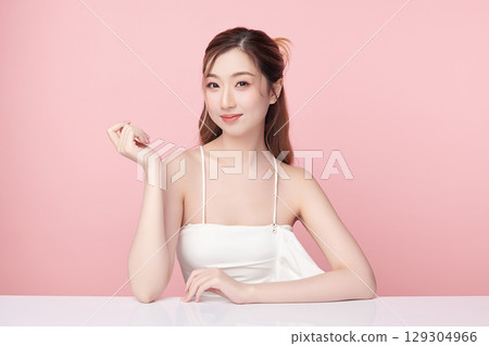 A beautiful young Asian woman with clean, fresh skin against a pink background. Skincare, facial treatment, cosmetology, beauty, and spa. An elegant portrait of an Asian woman. 129304966