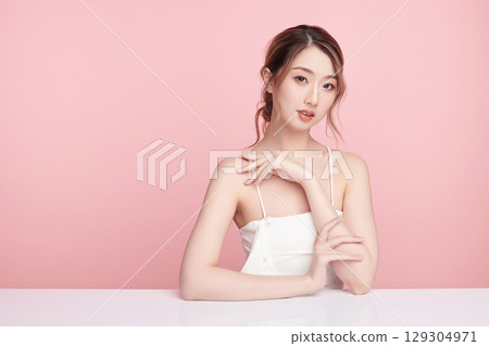 A beautiful young Asian woman with clean, fresh skin against a pink background. Skincare, facial treatment, cosmetology, beauty, and spa. An elegant portrait of an Asian woman. A beautiful young Asian woman with clean, fresh skin against a pink background. Skincare, facial treatment, cosmetology, beauty, and spa. An elegant portrait of an Asian woman. 129304971