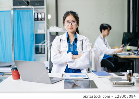 Confident young male doctor in white medical uniform sit at desk working on computer. Smiling use laptop 129305094
