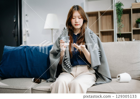Young Asian woman suffering from flu symptoms, covered with a blanket on a sofa. Concept of illness, healthcare 129305133