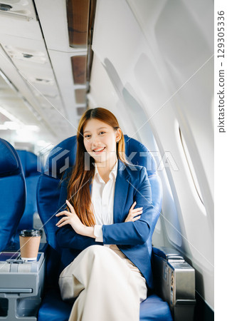 Asian female passenger of airplane sitting in comfortable seat while working laptop and tablet. Travel in style, 129305336
