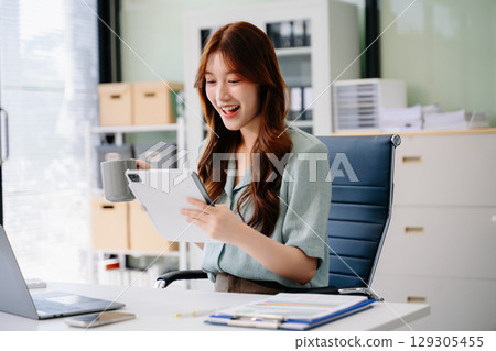 Beautiful Asian business woman typing laptop and tablet Placed at the table 129305455