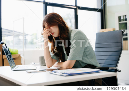 Asian woman feeling migraine head strain.Overworked businesswoman financier while working 129305484