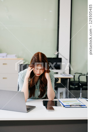 Asian woman feeling migraine head strain.Overworked businesswoman financier while working 129305485