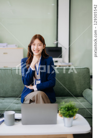 Young Asian working on laptops and tablets in a stylish office. Perfect for creativity, remote work, modern lifestyle Young Asian working on laptops and tablets in a stylish office. Perfect for creativity, remote work, modern lifestyle 129305542