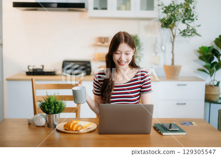 Happy woman with headphones working on a tablet in a bright kitchen. Ideal for themes of remote work 129305547