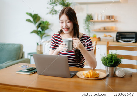 oung Asian woman with sitting working on laptops and tablets in a cozy workspace. Perfect for education, innovation, 129305548