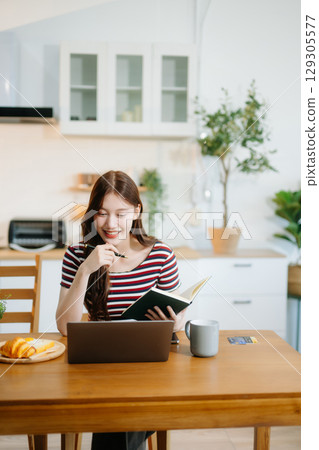 Happy woman with headphones working on a tablet in a bright kitchen. Ideal for themes of remote work 129305577