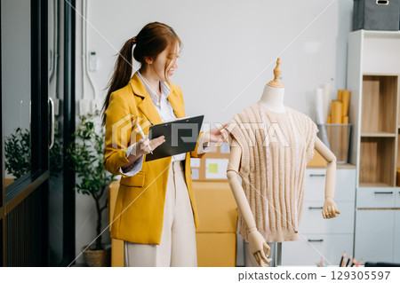 Asian tailor woman working on clothes in tailoring atelier. beautiful young female fashion designer smile Asian tailor woman working on clothes in tailoring atelier. beautiful young female fashion designer smile 129305597