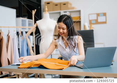 Asian young woman on desk in office of fashion designer and holds tablet, laptop and smartphone Asian young woman on desk in office of fashion designer and holds tablet, laptop and smartphone 129305725