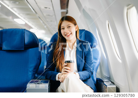 Asian female passenger of airplane sitting in comfortable seat while working laptop and tablet. Travel in style, 129305780