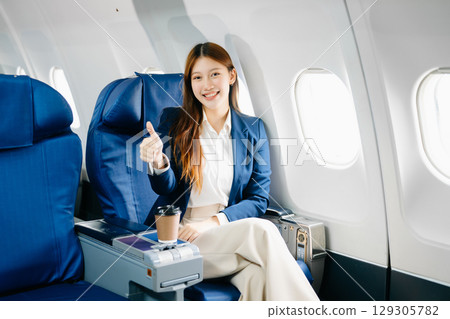 Asian female passenger of airplane sitting in comfortable seat while working laptop and tablet. Travel in style, Asian female passenger of airplane sitting in comfortable seat while working laptop and tablet. Travel in style, 129305782
