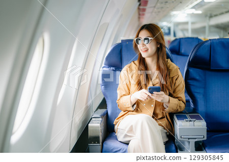 Smiling woman in first-class airplane seat, showcasing luxury, comfort, and elegance in travel. 129305845