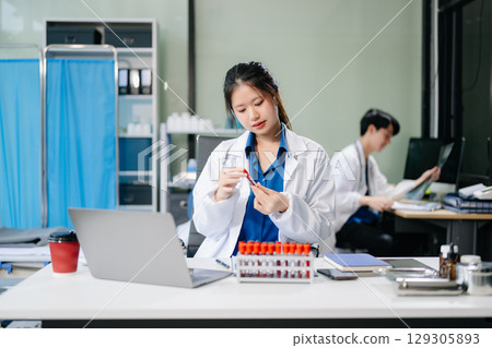 Confident young asian female doctor in white medical uniform sit at desk working on computer. 129305893