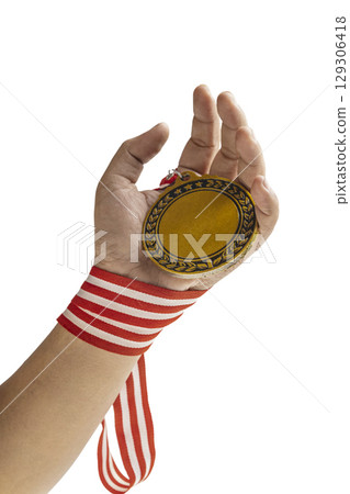 Human hand holding golden award medal suspended from a red and white striped ribbon isolated over a white background. Copy space. Symbol of achievement, recognition, or competition 129306418