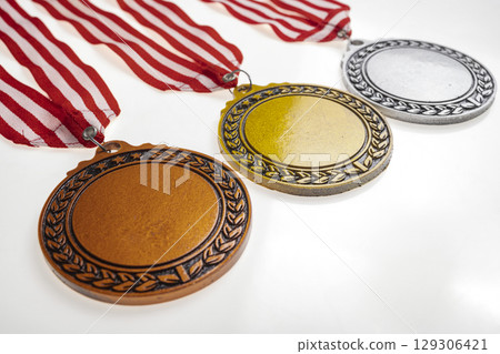Set of the bronze, silver, and golden award medals suspended from a red and white striped ribbon isolated over a white background. Copy space. Symbol of achievement, recognition, or competition 129306421