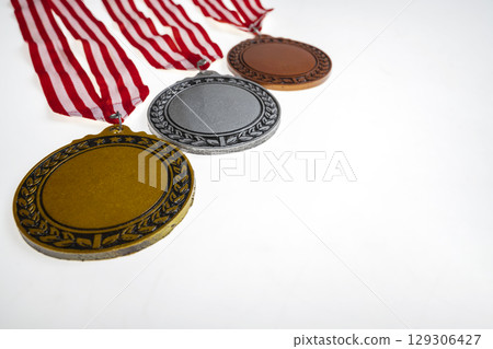 Set of the bronze, silver, and golden award medals suspended from a red and white striped ribbon isolated over a white background. Copy space. Symbol of achievement, recognition, or competition 129306427