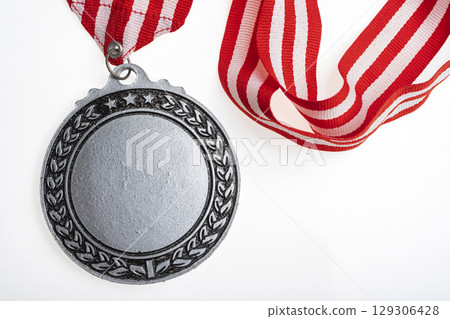 Closeup view of the silver award medal suspended from a red and white striped ribbon isolated over a white background. Copy space. Symbol of achievement, recognition, or competition Closeup view of the silver award medal suspended from a red and white striped ribbon isolated over a white background. Copy space. Symbol of achievement, recognition, or competition 129306428