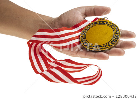 Human hand holding golden award medal suspended from a red and white striped ribbon isolated over a white background. Copy space. Symbol of achievement, recognition, or competition 129306432