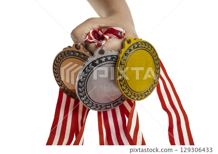 Human hand holding set of bronze, silver and golden award medals suspended from a red and white striped ribbon isolated white background. Copy space. Symbol of achievement, recognition, or competition Human hand holding set of bronze, silver and golden award medals suspended from a red and white striped ribbon isolated white background. Copy space. Symbol of achievement, recognition, or competition 129306433