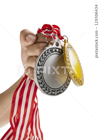 Human hand holding silver and golden award medals suspended from a red and white striped ribbon, isolated over a white background. Copy space. Symbol of achievement, recognition, or competition 129306434
