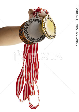 Human hand holding set of bronze, silver and golden award medals suspended from a red and white striped ribbon isolated white background. Copy space. Symbol of achievement, recognition, or competition 129306435