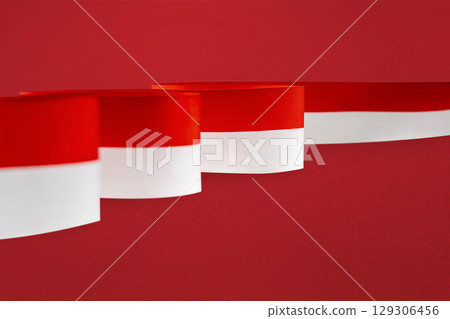 The striped red and white ribbon of the Indonesian flag on a red background. Concept of Indonesian Independence Day or Kemerdekaan The striped red and white ribbon of the Indonesian flag on a red background. Concept of Indonesian Independence Day or Kemerdekaan 129306456