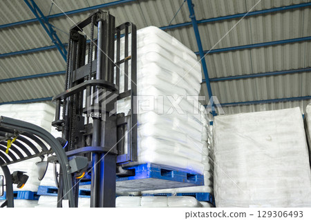 Forklift lifts a stacked white sack in a warehouse. Storage, inventory, industry, and logistics 129306493