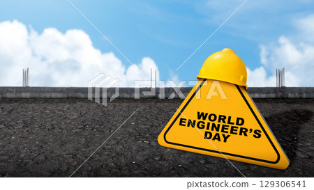 Yellow hard hat safety equipment with the message of World Engineer Day on a yellow sign with a construction site background. Concept of World Engineer Day Yellow hard hat safety equipment with the message of World Engineer Day on a yellow sign with a construction site background. Concept of World Engineer Day 129306541