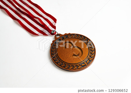 Closeup view of the 3rd bronze award medal suspended from a red and white striped ribbon isolated over a white background. Symbol of achievement, recognition, or competition Closeup view of the 3rd bronze award medal suspended from a red and white striped ribbon isolated over a white background. Symbol of achievement, recognition, or competition 129306652