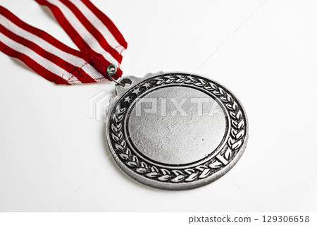Closeup view of the silver award medal suspended from a red and white striped ribbon isolated over a white background. Copy space. Symbol of achievement, recognition, or competition Closeup view of the silver award medal suspended from a red and white striped ribbon isolated over a white background. Copy space. Symbol of achievement, recognition, or competition 129306658