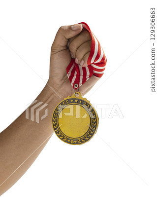 Human hand holding golden award medal suspended from a red and white striped ribbon isolated over a white background. Copy space. Symbol of achievement, recognition, or competition 129306663