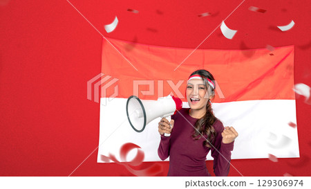 Indonesian southeast asian woman celebrating Indonesia Independence Day on the 17th of August, holding a megaphone with the Indonesian national flag. Concept of Kemerdekaan Indonesia 129306974