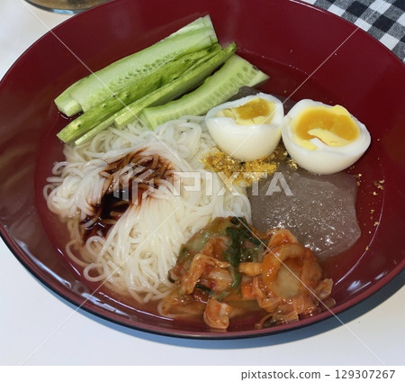 Cold and refreshing Korean naengmyeon noodles, served in a chilled broth with sliced cucumber, radish, and a boiled egg. A savory, tangy dish ideal for hot summer days. 129307267