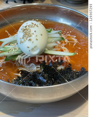 Cold and refreshing Korean naengmyeon noodles, served in a chilled broth with sliced cucumber, radish, and a boiled egg. A savory, tangy dish ideal for hot summer days. 129307293
