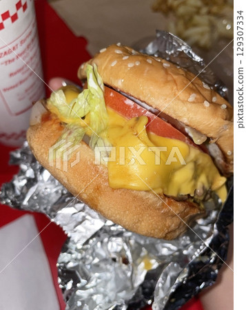 A mouthwatering burger with a juicy patty, fresh lettuce, tomato, and melted cheese, all nestled in a soft bun. Perfect for food photography, showcasing the indulgence of classic comfort food. 129307334