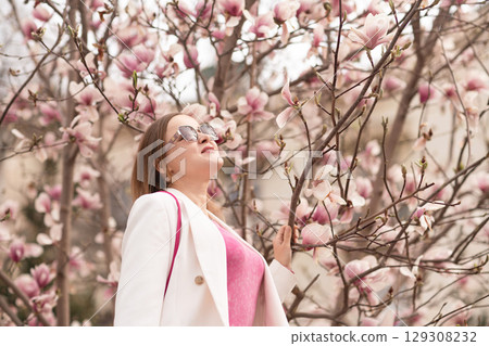 Magnolia Bloom Woman: Springtime lady looks up at pink flowers in park enjoying beauty. 129308232