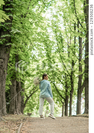 Flowers Woman Park: Lady with bouquet walks in sunlit park in daytime for nature enjoyment. 129308236