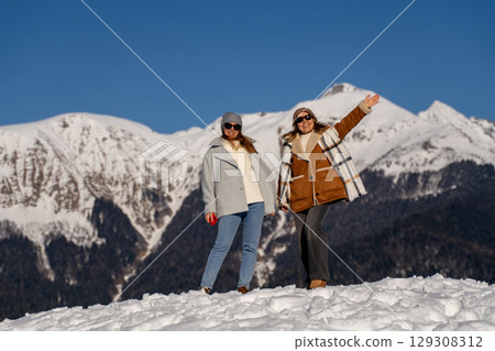 Mountains Women Winter: Snowy peak adventure; cheerful friends pose joyfully, sunny day. 129308312