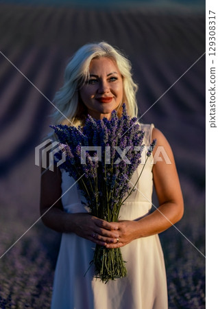 Blonde woman poses in lavender field at sunset. Happy woman in white dress holds lavender bouquet. Aromatherapy concept, lavender oil, photo session in lavender Blonde woman poses in lavender field at sunset. Happy woman in white dress holds lavender bouquet. Aromatherapy concept, lavender oil, photo session in lavender 129308317