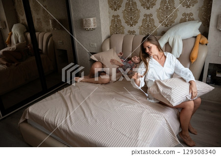 Woman, Child, Bedroom: Mother making bed, child on bed, morning routine, domestic scene, home. Woman, Child, Bedroom: Mother making bed, child on bed, morning routine, domestic scene, home. 129308340